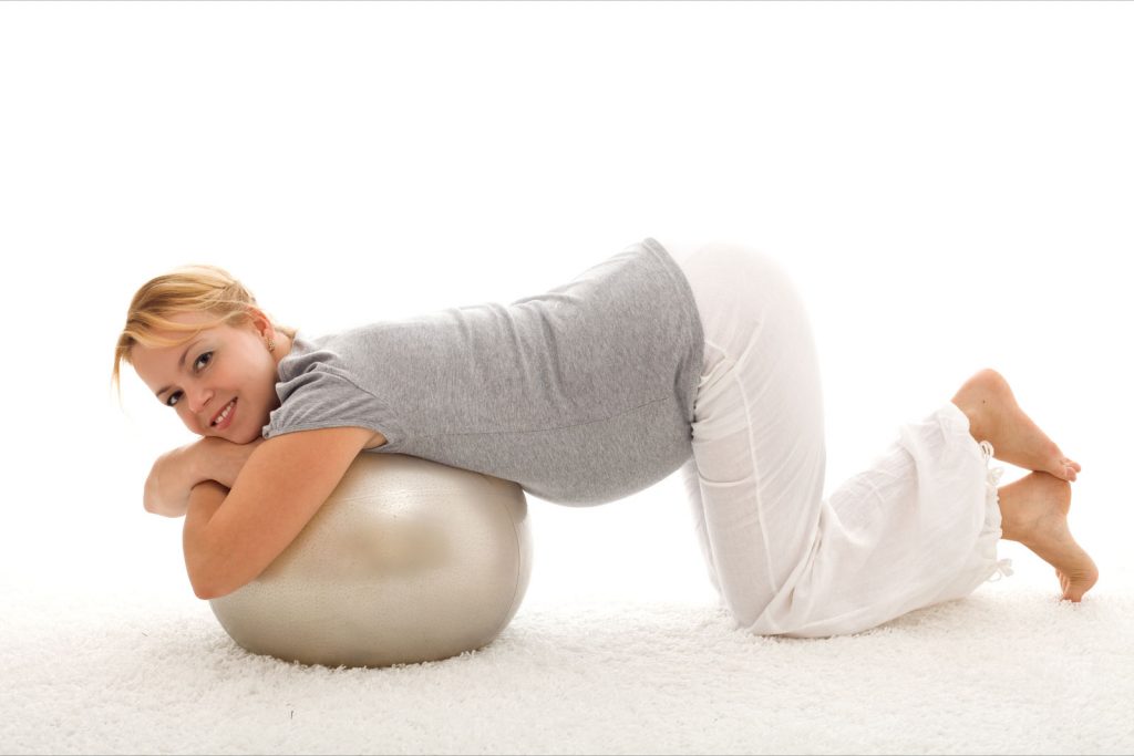 Beautiful woman exercising with large ball kneeling on the floor indoors - isolated